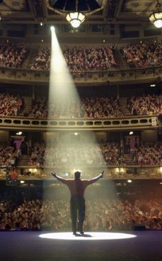 a man standing on top of a stage with his arms wide open in front of an audience