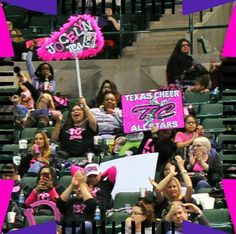 a group of people sitting in the stands at a baseball game holding up pink signs