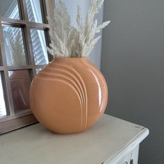 a vase sitting on top of a dresser next to a window with a plant in it