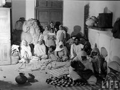 black and white photograph of people sitting on the floor in a room with many pots