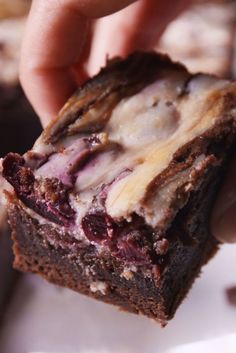 a hand holding a piece of brownie with white chocolate and cherries