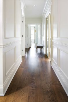 an empty hallway with hard wood flooring and white trim on the walls is seen in this image