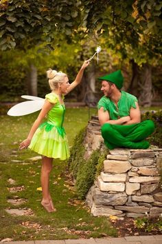 a man and woman dressed as tinkerbells sitting on a stone wall in the park