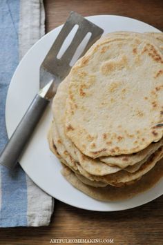 a stack of tortillas sitting on top of a white plate next to a fork