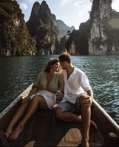 a man and woman sitting on the back of a boat in front of some mountains