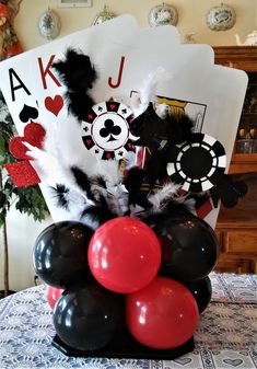 black and red balloons in a vase on a table with playing card cards behind it