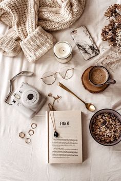 an open book, camera, and other items on a bed with white linens