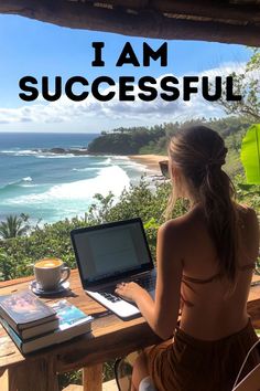 a woman sitting at a table with a laptop on her lap looking out over the ocean