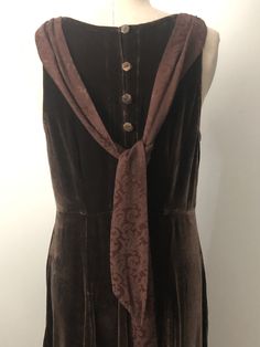 This is a stunning brown velvet dress hand created by Jane Mohr for Dress to Kill. The dress is accented with a jacquard print tie that can worn in the front or back of the dress. The dress closes with 5 flower shaped shell buttons. This dress has a fun 20's vibe. No content or size tag. Check measurements carefully, no stretch. Measurements taken with dress laying flat and doubled where appropriate. In order to determine fit we recommend comparing measurements with an item that fits you well. L Formal Sleeveless Brown Maxi Dress, Sleeveless Brown Maxi Dress For Formal Occasions, Brown Sleeveless Maxi Dress For Formal Occasions, Brown Long Dress For Formal Occasions, Brown Formal Maxi Dress For Fall, Brown Maxi Dress For Formal Fall Occasions, Fall Formal Brown Maxi Dress, Elegant Brown Velvet Dress, Brown Velvet Dress