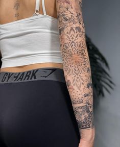 a woman's arm with tattoos on it and a white tank top behind her