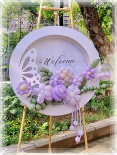 a welcome sign with flowers and butterflies on it in front of a tree filled area