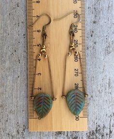 a pair of leaf shaped earrings sitting on top of a wooden board next to a measuring ruler