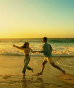 two people running on the beach at sunset with waves coming in and one person holding his hand