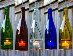 four different colored bottles with candles in them hanging on a chain next to a fence