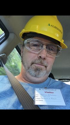 a man wearing a yellow hard hat and glasses sitting in a car with a certificate on his lap