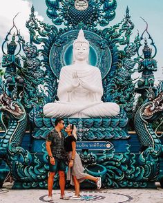 two people standing in front of a large buddha statue