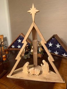 a nativity scene with three wooden christmas trees and an american flag in the background