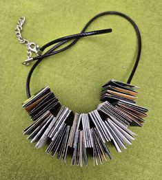 a necklace made out of magazines on a green surface with a black cord and silver beads