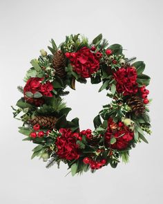 a christmas wreath with red flowers and pine cones on white background, decorated with greenery