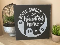 a sign that says home sweet and has two ghost faces on it, sitting next to a potted plant