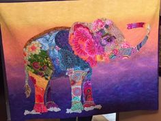 an elephant made out of fabric is displayed on a tablecloth with purple, yellow and orange colors