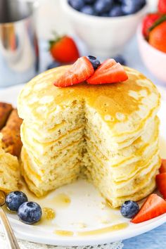 a stack of pancakes on a plate with blueberries and strawberries next to it