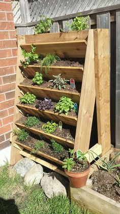 a wooden shelf filled with potted plants next to a brick building and grass covered ground