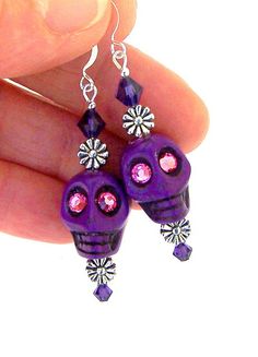 a pair of purple skull earrings with pink crystals