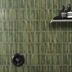 a bathroom with green tile and black shower faucet next to shelf on the wall