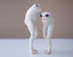 two white plastic figures with eyes and arms touching each other's foreheads on a table