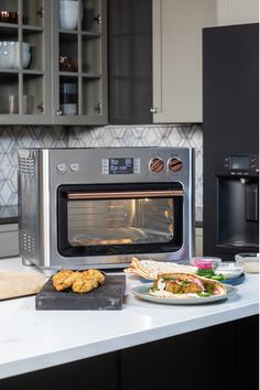 a stainless steel oven with food in front of it on a kitchen countertop next to a plate of cookies