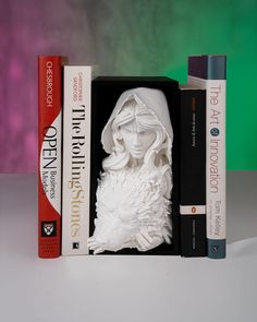 two books are sitting next to each other in front of a bookend that has a statue of a woman's head on it