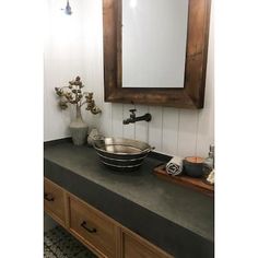 a bathroom sink sitting under a mirror next to a wooden counter top with drawers underneath it