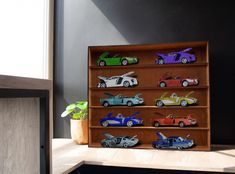 a wooden shelf filled with toy cars next to a potted plant