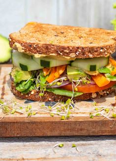 a sandwich with lettuce, carrots and cucumbers on a cutting board