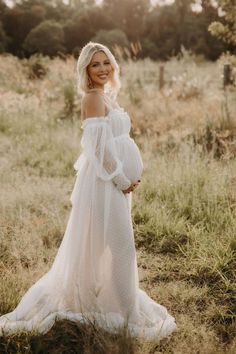 a pregnant woman wearing a white dress standing in a field