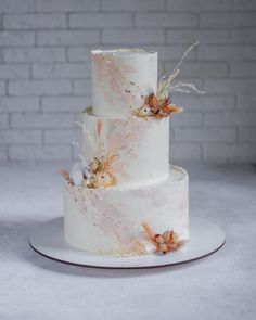 a three tiered wedding cake with flowers on top is displayed in front of a brick wall