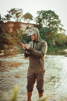 a man standing in the water while holding a fishing rod and wearing a hoodie