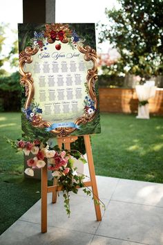 an easel with a wedding seating chart on it in front of some grass and flowers