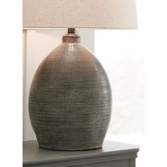 a gray vase sitting on top of a table next to a lampshade with a beige shade