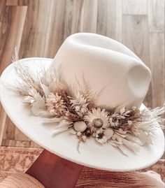 a white hat with flowers and feathers on it sitting on top of a wooden floor