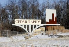 a sign that reads cedar rapids in front of some trees and bushes with snow on the ground