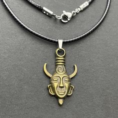 two necklaces one with a gold mask and the other has a black leather cord