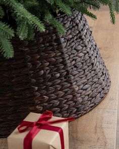 a christmas tree in a basket next to a present box with a red ribbon on it