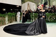 a woman in a black gown standing on a white floor with people taking pictures behind her