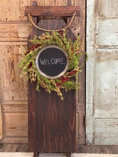 a welcome sign hanging on the side of a wooden door with a wreath around it