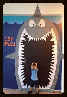 a young boy standing in front of a giant shark poster