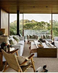 a living room filled with lots of furniture next to a large glass window covered in trees