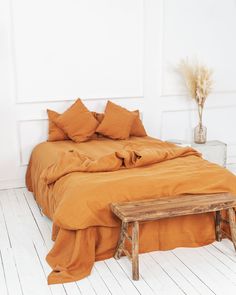 a bed with orange sheets and pillows in a white room next to a wooden bench