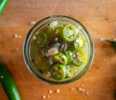 a jar filled with pickles on top of a wooden table next to green peppers